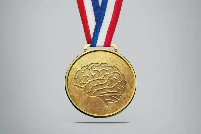 Photo sur fond blanc. Gros plan d'une médaille d'or sur laquelle est gravé le dessin d'un cerveau. Le ruban de la médaille est bleu blanc rouge.