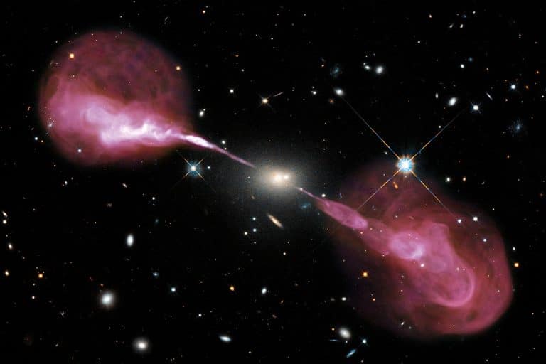 Photo prise dans l'espace. Fond noir. Plusieurs astres un peu partout. Au centre de l'image, un point lumineux blanc avec un halo. De part et d'autre de ce point, des nuages roses.